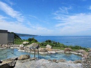 A clear pool with rocks and a metal chair, surrounded by a stone deck, overlooking a body of water and distant land.