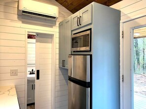 Une cuisine avec des meubles blancs, un réfrigérateur en acier inoxydable, un four et un appareil de climatisation.