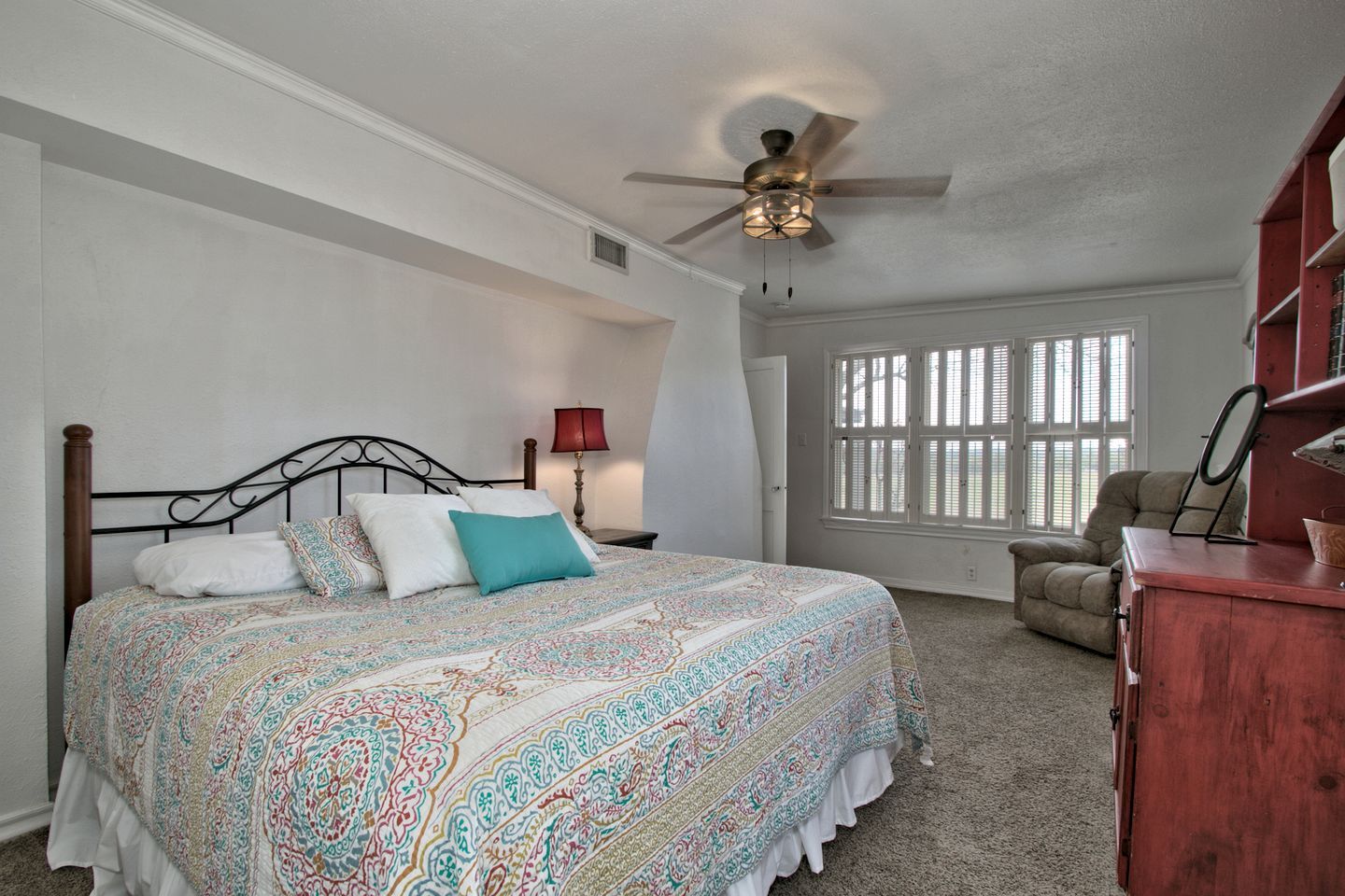 A bedroom with a bed, a ceiling fan, a window with blinds, a chair, and a dresser.