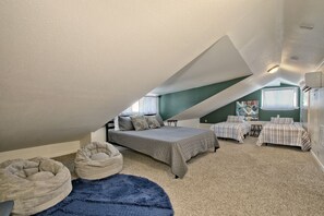 Une chambre avec un plafond en pente, deux lits, un fauteuil en forme de poire et un tableau au mur.
