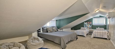 A bedroom with a sloped ceiling, two beds, a bean bag chair, and a painting on the wall.