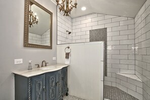 A bathroom with a white vanity, a large mirror, a chandelier, and a shower area with patterned tiles.