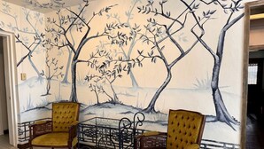 Una habitación con dos sillones tapizados en amarillo, una mesita y un mural con árboles y un paisaje.