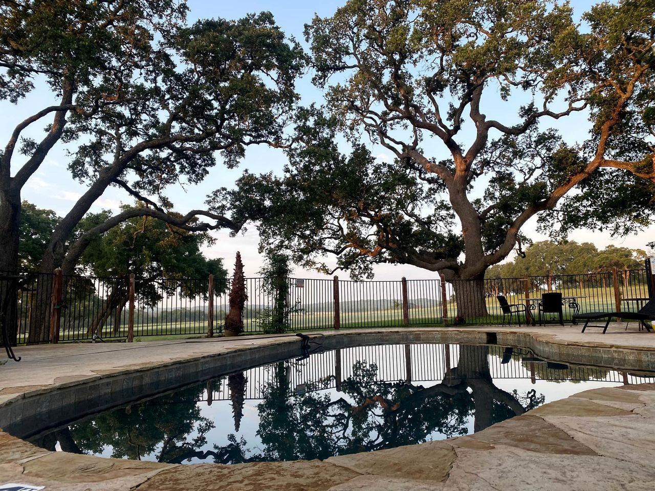 Piscina rodeada de árboles y un área cercada con mobiliario exterior.