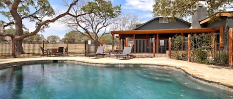 A clear swimming pool with lounge chairs and a covered patio area.