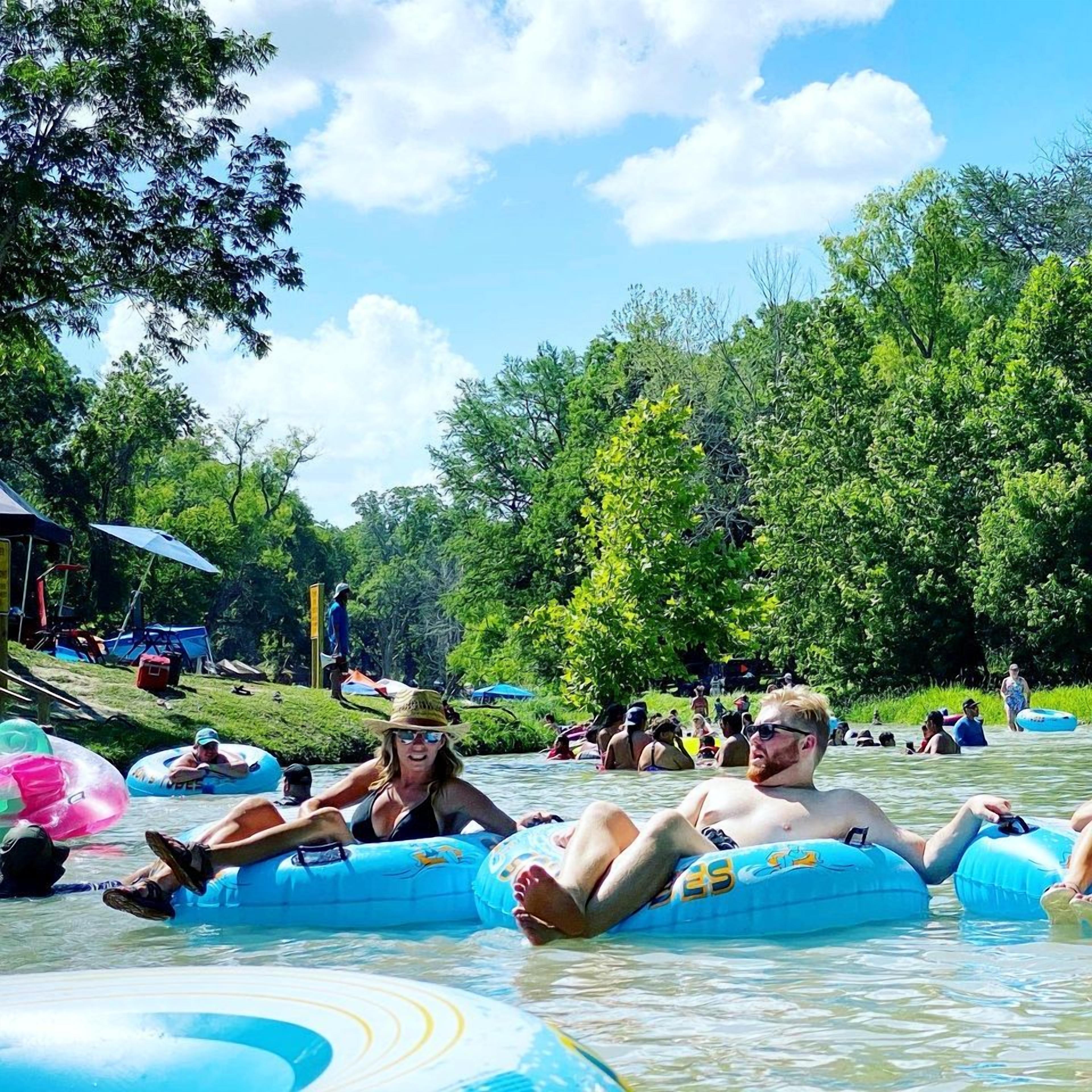Des personnes flottant sur l’eau dans un environnement naturel, avec des arbres et un ciel dégagé.