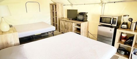 Una sistemazione in tenda con un letto, una televisione, un forno a microonde e un angolo cottura.
