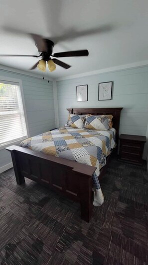A bedroom with a bed, a ceiling fan, a nightstand, and a window.