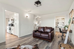 Una sala moderna con un sofá de cuero, un comedor con una mesa de madera y una cocina con gabinetes blancos.
