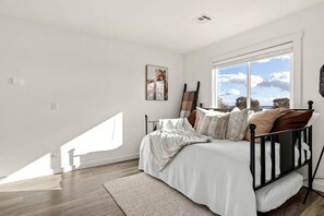 A bedroom with a bed, a window, and a painting on the wall.