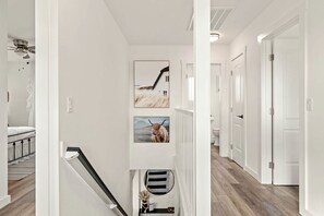 Un couloir aux murs blancs, doté d’un plancher en bois et d’un escalier avec une rampe noire.