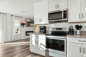 A modern kitchen with white cabinets, a built-in microwave, a coffee maker, and a fireplace.