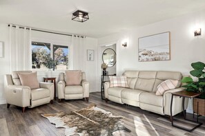 A living room with a beige sofa, two armchairs, a rug, and a large window with curtains.