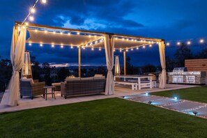 Un patio exterior con luces colgantes, una parrilla y un área de estar con un sofá y sillas.
