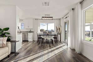 A modern kitchen with white cabinets, a dining area with a wooden table and chairs, and a large window offering a view.