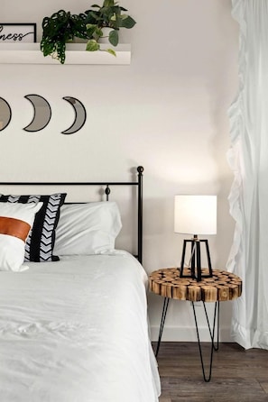 A neatly made bed with white bedding, a black metal headboard, and a round wooden side table with a lamp.