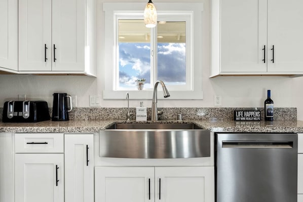 A kitchen with white cabinets, a stainless steel sink, a toaster, a coffee maker, and a wine bottle.