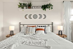 A neatly made bed with white bedding, two bedside tables with lamps, a wall-mounted shelf with plants, and a decorative moon sign. - Heavenly Vacation Retreat with Sweeping Vineyard Views near Paso Robles Wineries in California (Paso Robles)