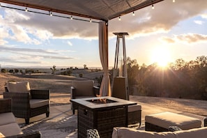 Un patio al aire libre con mobiliario de mimbre, un hogar para fogata y vistas del paisaje.