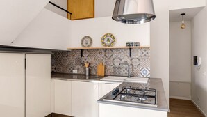 Una cucina moderna con mobili bianchi, piano cottura a gas, cappa aspirante in acciaio inossidabile e piatti decorativi su uno scaffale.