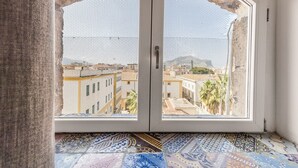 Una stanza con un'ampia finestra ad arco che si affaccia su una vista urbana, pavimento in piastrelle decorate e una porta provvista di zanzariera.