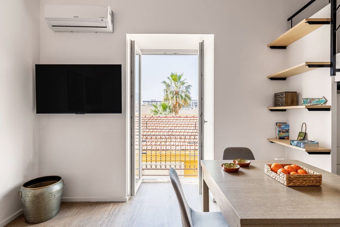 Een moderne keuken met een eetgedeelte, een aan de muur bevestigde televisie en een uitzicht op de stad door de open deur.