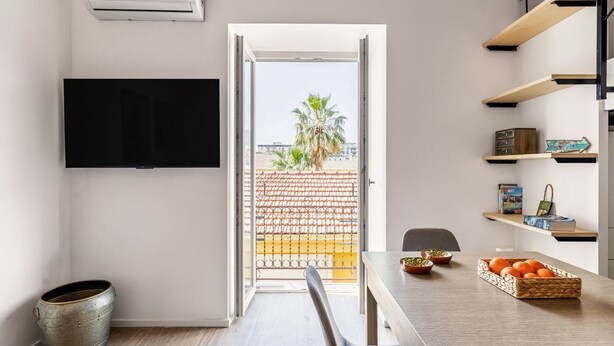 Una cucina moderna con zona pranzo, TV a parete e vista sulla città attraverso l'ingresso aperto.