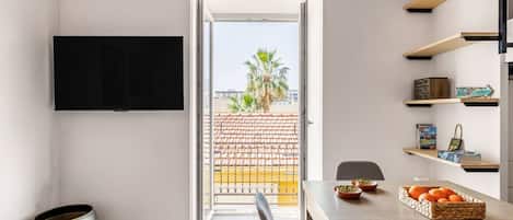 Een moderne keuken met een eetgedeelte, een aan de muur bevestigde televisie en een uitzicht op de stad door de open deur.
