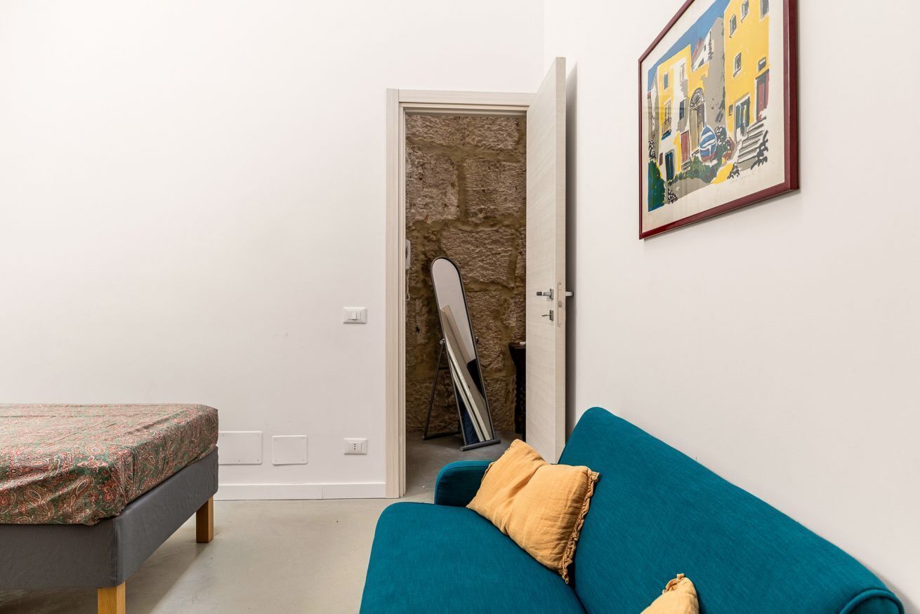 Una habitación con una cama, un sofá azul, un cuadro y una puerta que da a una pared de piedra.