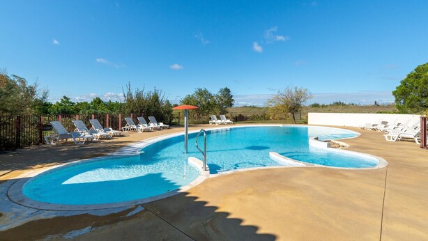 Una piscina amb gandules i un parasol vermell, envoltada per una tanca i arbres.