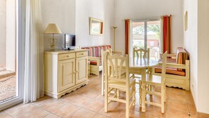 Habitació amb taula de dinar, cadires, televisió sobre un moble, sofà i finestra amb cortines.