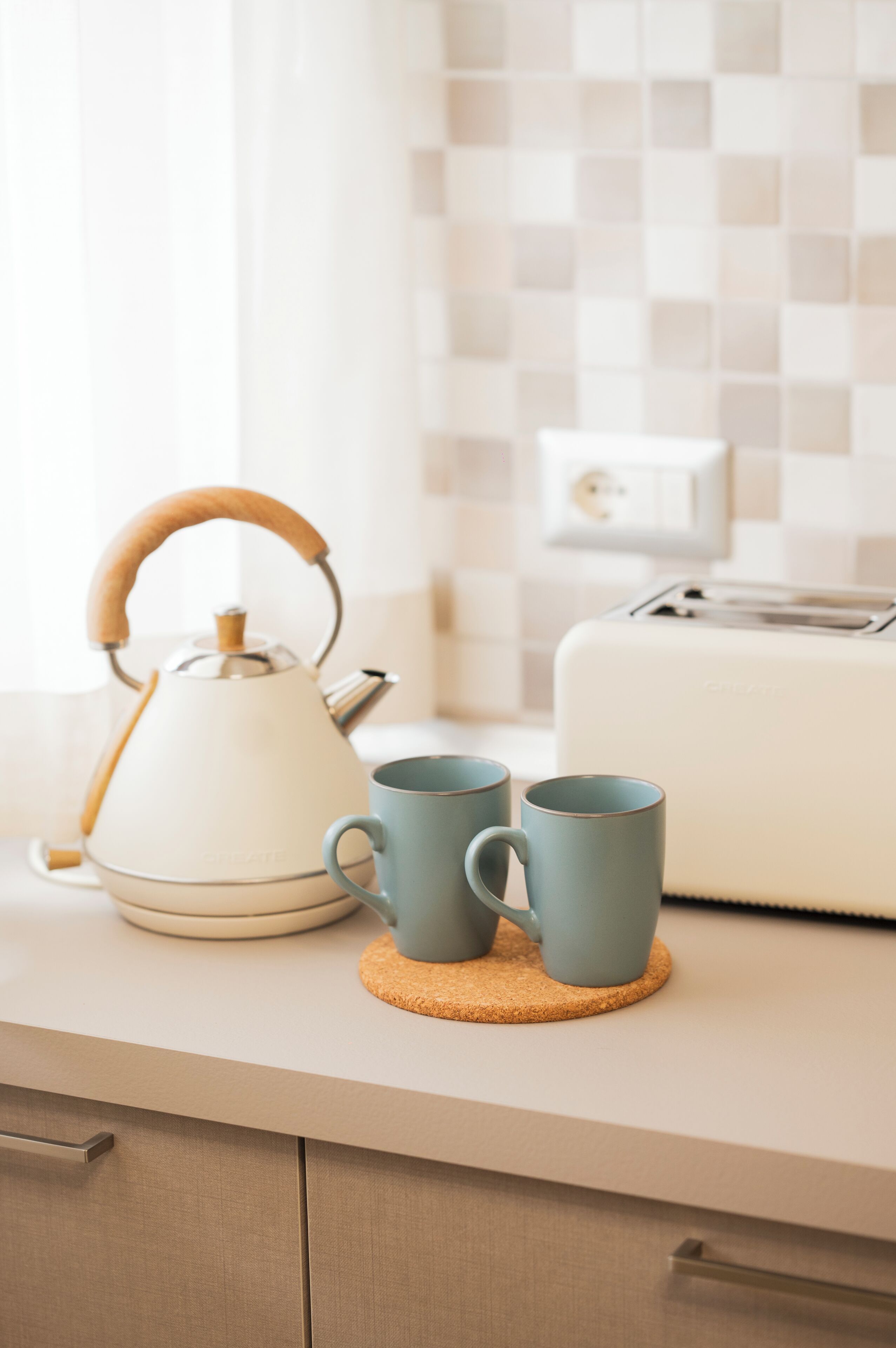 Una encimera de cocina con un hervidor, dos tazas y un tostador.