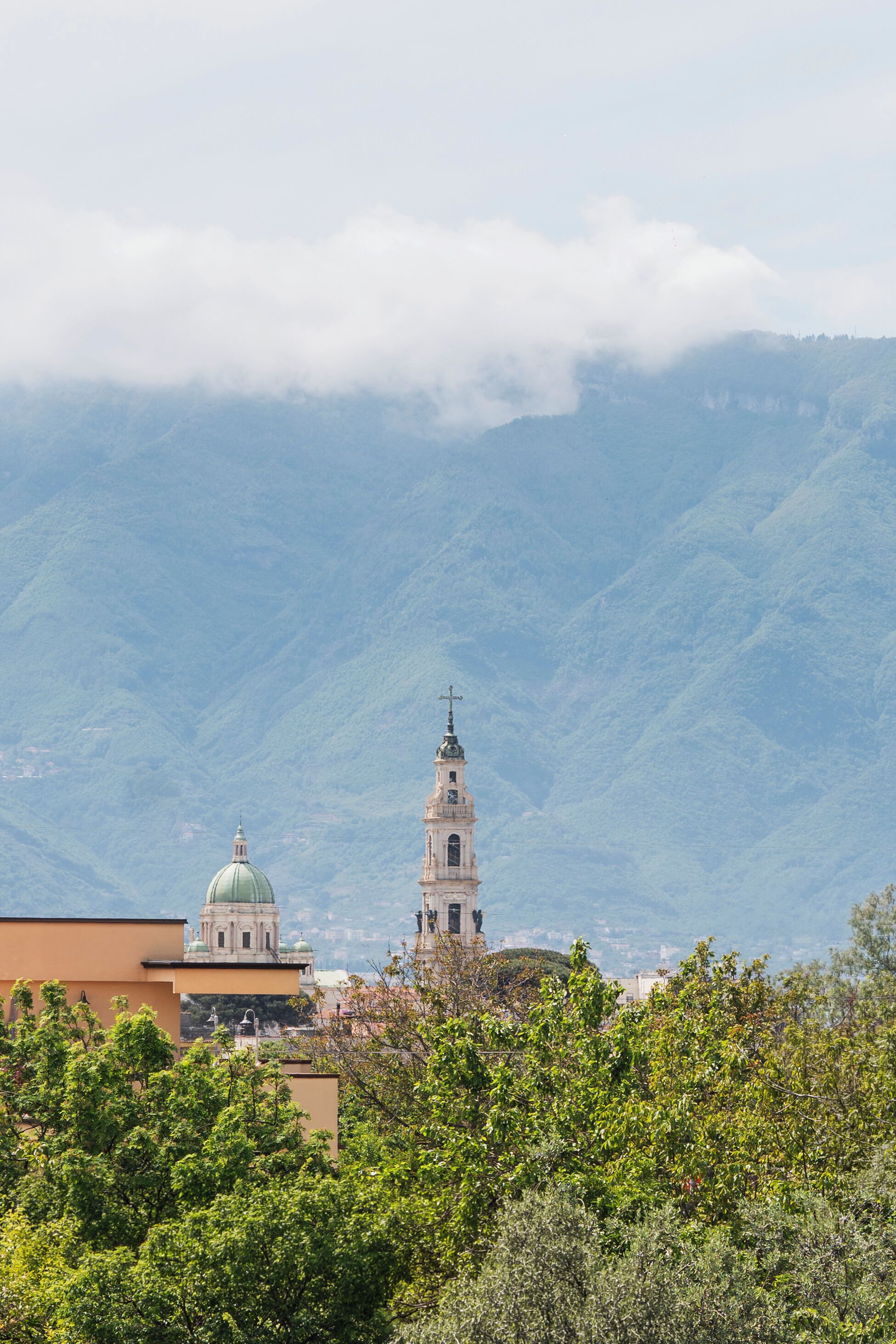 Una chiesa con campanile e cupola, circondata dal verde e dalle montagne.