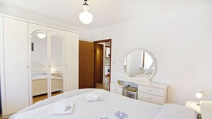 Un dormitorio con cama, armario, tocador con espejo y mesita de noche.