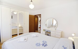 A bedroom with a bed, a wardrobe, a vanity with a mirror, and a bedside table.