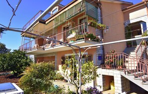 A multi-story residential building with balconies, potted plants, and a visible staircase.