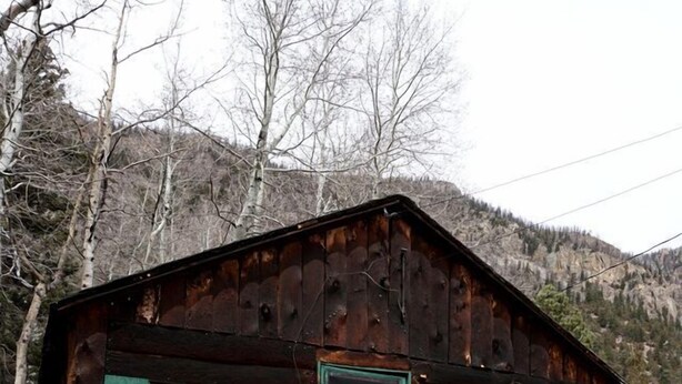 En enkel stuga med en rustik känsla, träfasad, en grön dörr och en liten veranda.