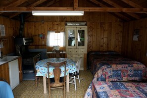 Interior de cabana amb decoració de fusta, una taula amb estovell de disseny, un armari, un llit amb matalàs i una finestra amb cortines.