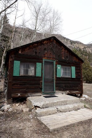 A rustic cabin with a wooden exterior, a green door, and a small porch. - Remote and Off-Grid Cabin in Poudre Canyon, Perfect for a Fishing Retreat (Bellvue)