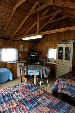 Eine Hütte mit Holzvertäfelung, einem Esstisch, zwei Stühlen, einem Schrank und einem Bett mit gemustertem Bettbezug.