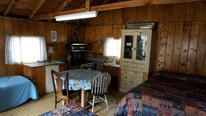 Ett rum i stugliknande stil med två sängar, ett matbord, ett litet kök och ett skåp.