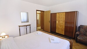Een slaapkamer met een bed, een kledingkast, een spiegel, een nachtkastje met een lamp en een stoel.