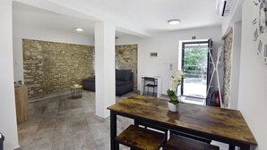 Un interior moderno con una pared de piedra, una mesa de madera con una orquídea en maceta, un sofá gris y una escalera que conduce a un espacio exterior.