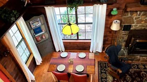 Un coin repas avec une table en bois dressée pour quatre personnes, une lampe suspendue et une vue par la fenêtre.
