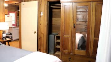 A wooden room with a bed, a wardrobe, a desk with a lamp, and a small table.