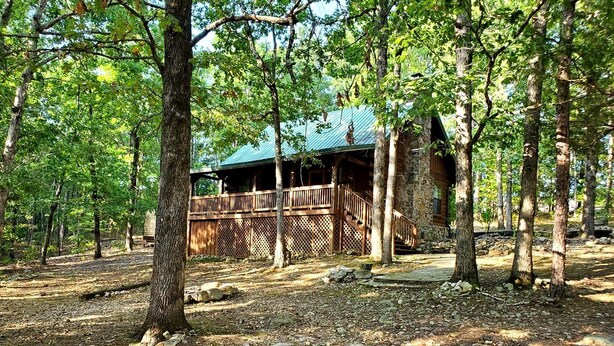 Un chalet rustique doté d’une terrasse en bois et d’un toit en métal, entouré d’arbres.