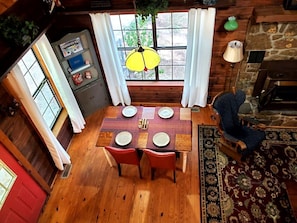 Un coin repas avec une table en bois dressée pour quatre personnes, une lampe suspendue et une vue par la fenêtre.