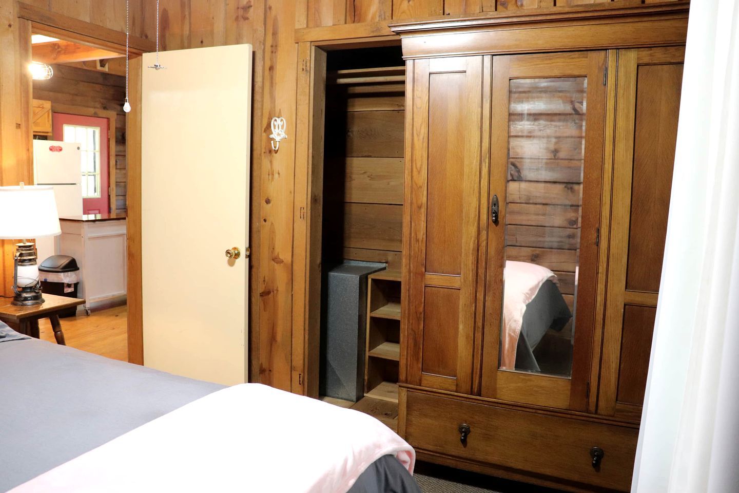 Quarto de madeira com uma cama, um guarda-roupa, uma escrivaninha com uma luminária e uma mesinha.