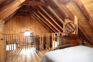 Ein Zimmer mit Holzeinrichtung, einem Bett, einer Hängeleuchte und einer Holztreppe.