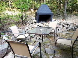Ein Außenbereich mit Sitzgelegenheit, einem Steinkamin und Metallstühlen.